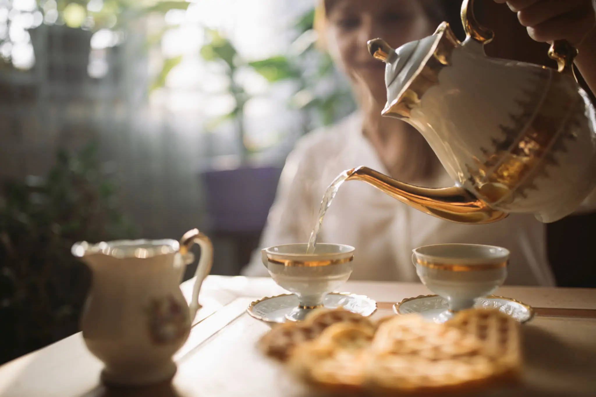 Hand pouring tea into gold-rimmed teacups